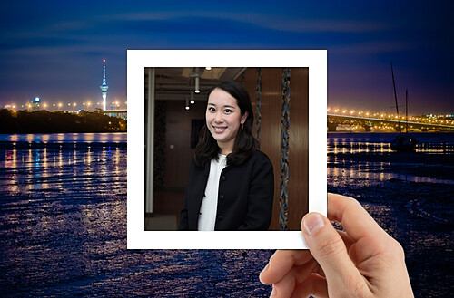 A hand holds a photo of four smiling people taking a selfie, with a vibrant city nightscape in the background.