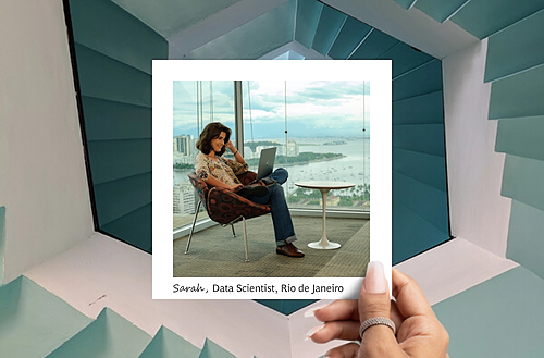 A Polaroid-style photograph features a woman named Sarah, a Data Scientist from Rio de Janeiro. She is sitting in a modern, stylish chair in front of a large window with a panoramic view of the city and coastline. Sarah is focused on her laptop, dressed in casual professional attire with jeans and a patterned top. A small round table is next to her. The Polaroid is held up against a background of a geometric, blue and white architectural structure, with the caption "Sarah, Data Scientist, Rio de Janeiro" written at the bottom of the photo. 