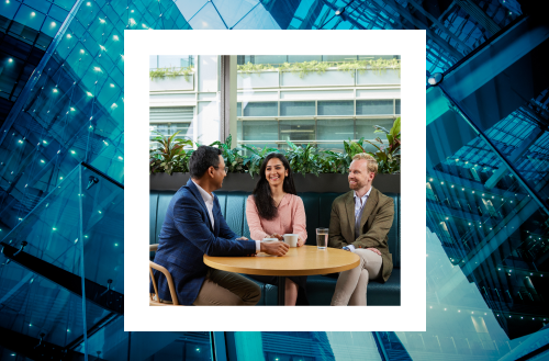 A photo of three professionals in a casual meeting outdoors, with a backdrop of a glass building and greenery, framed by a geometric blue structure.
