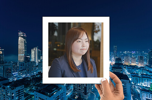 A hand holds a photo of four smiling people taking a selfie, with a vibrant city nightscape in the background.