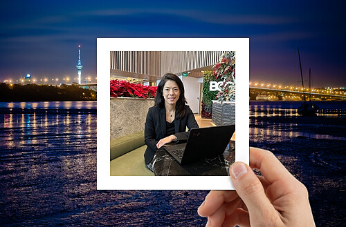 A hand holds a photo of four smiling people taking a selfie, with a vibrant city nightscape in the background.