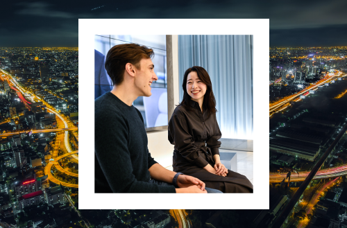 A photo of a man and woman smiling and conversing, set over a night cityscape with illuminated streets and buildings.